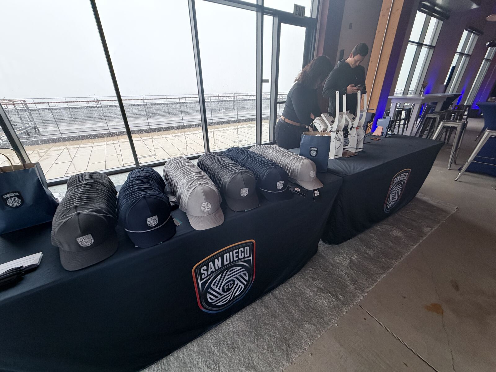 Branded hat display with multiple customized caps on a table with guests in the background